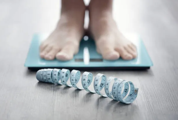 Medical Weight Loss - Express Internal Medicine Close-up of feet on a weight scale with a measuring tape, symbolizing medical weight loss journey in Plano, TX.